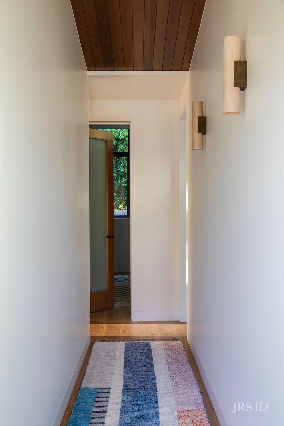 Hallway with custom runner, wood flooring, and modern wall sconces at the Eucalyptus Hill ADU Residence in Montecito.