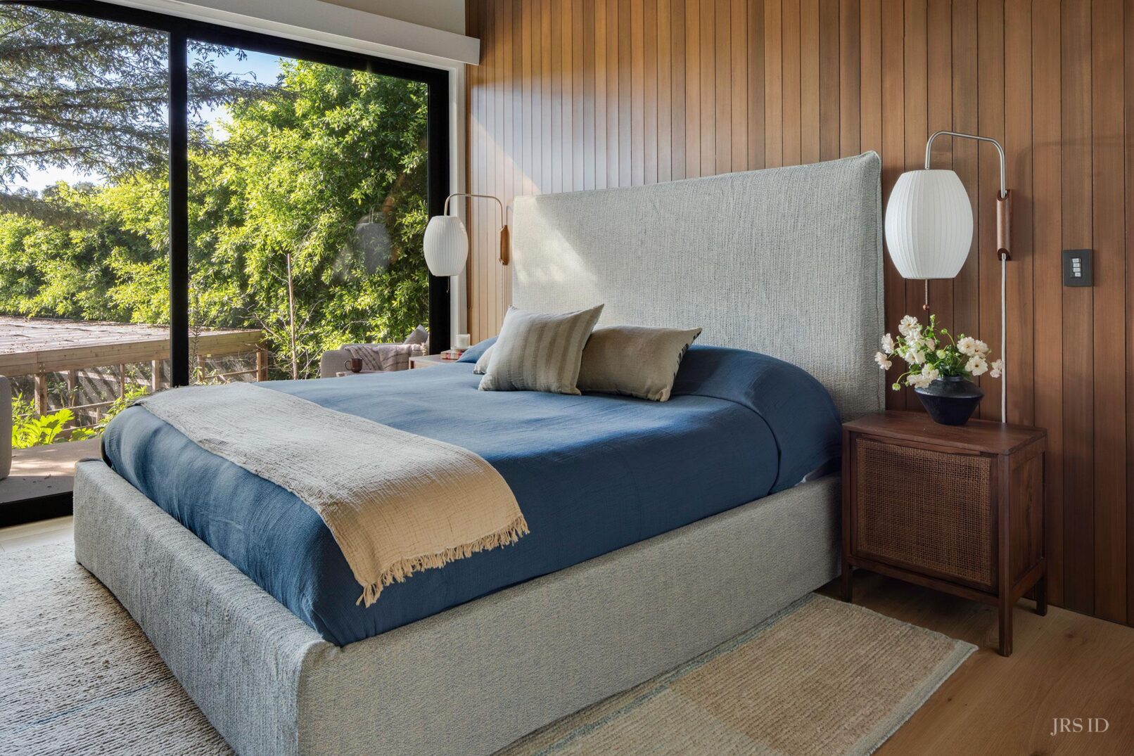 Primary bedroom with upholstered bed, wood accent wall, and garden views at the Eucalyptus Hill ADU Residence in Montecito